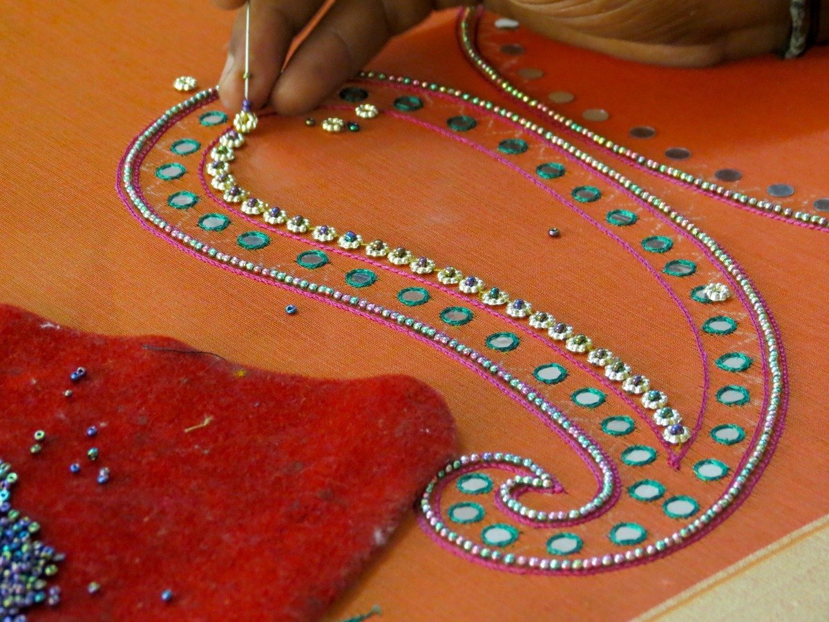 Professional boutique artisan handcrafting intricate gold zari and mirror embroidery on luxury silk